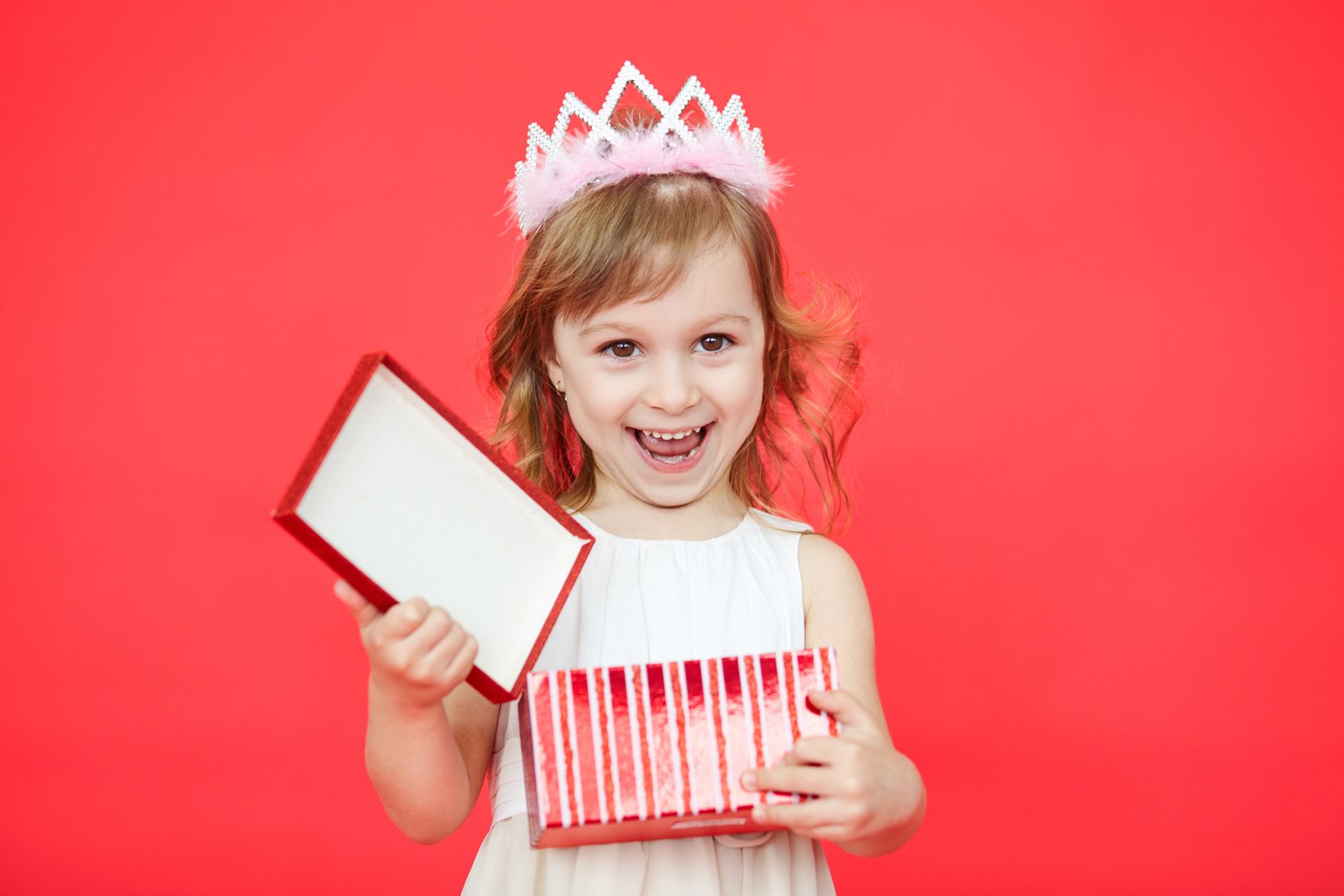 Happy Kid girl opening a gift box isolated on red background. Surprised cute little girl with a red wrapped present