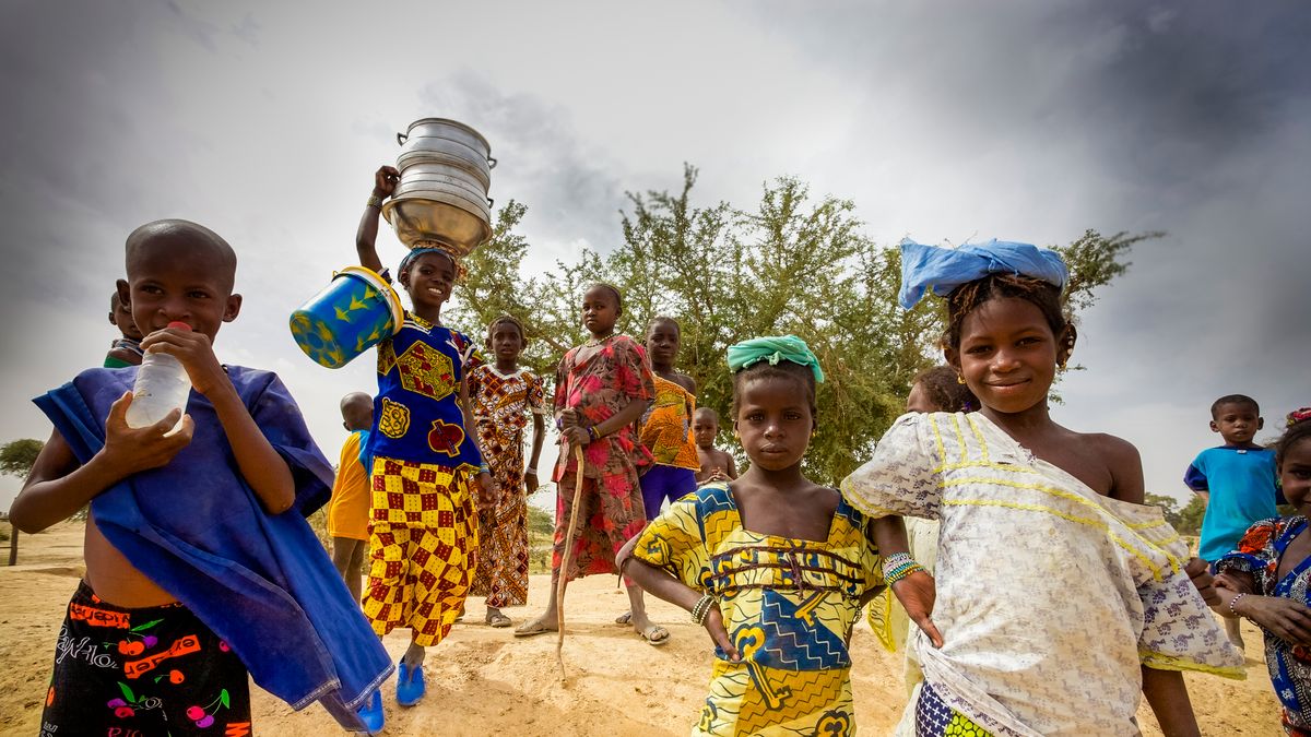 MOPTI, MALI - DEC 31: Unidentified kids walking in the countryside, a young girl is carrying kitchenware on her head, pure African tradition. Lifestyle around Mopti in Mali 2012.