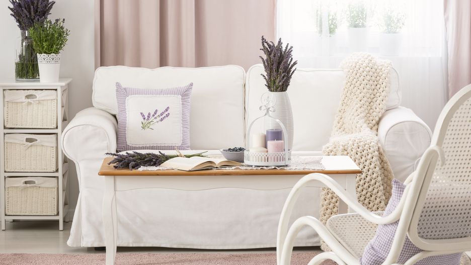 Wooden coffee table with pastel candles, fresh lavender and open book in real photo of bright sitting room interior with white couch