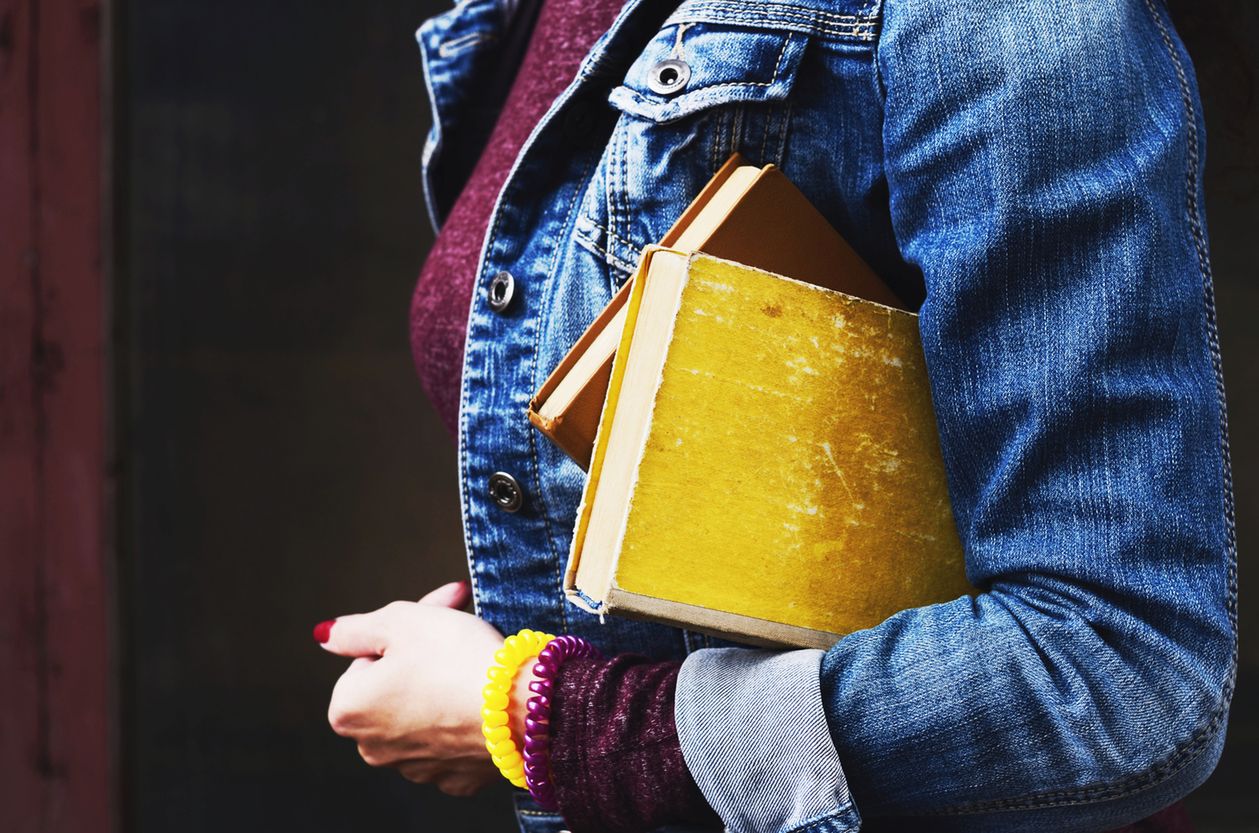 Young woman in jeans jacket holding pile of vintage books in her hand 