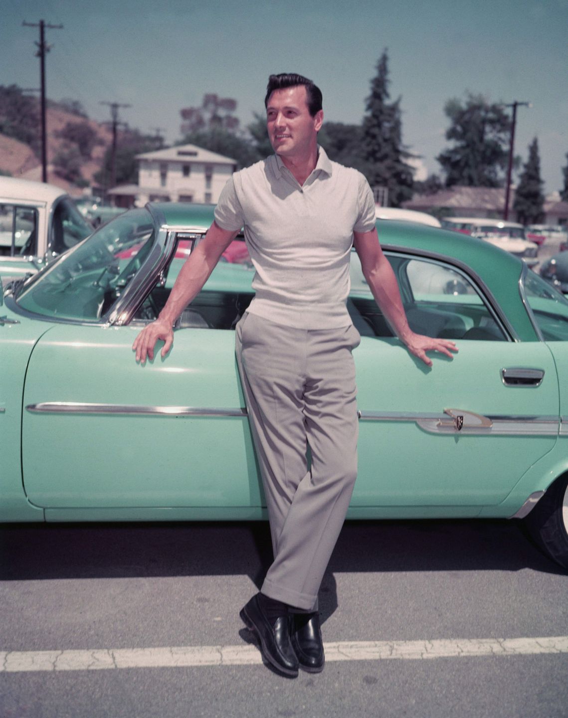 American actor Rock Hudon (1925 - 1985) leans against a sea foam green car in a parking lot, 1950s. (Photo by Getty Images) 