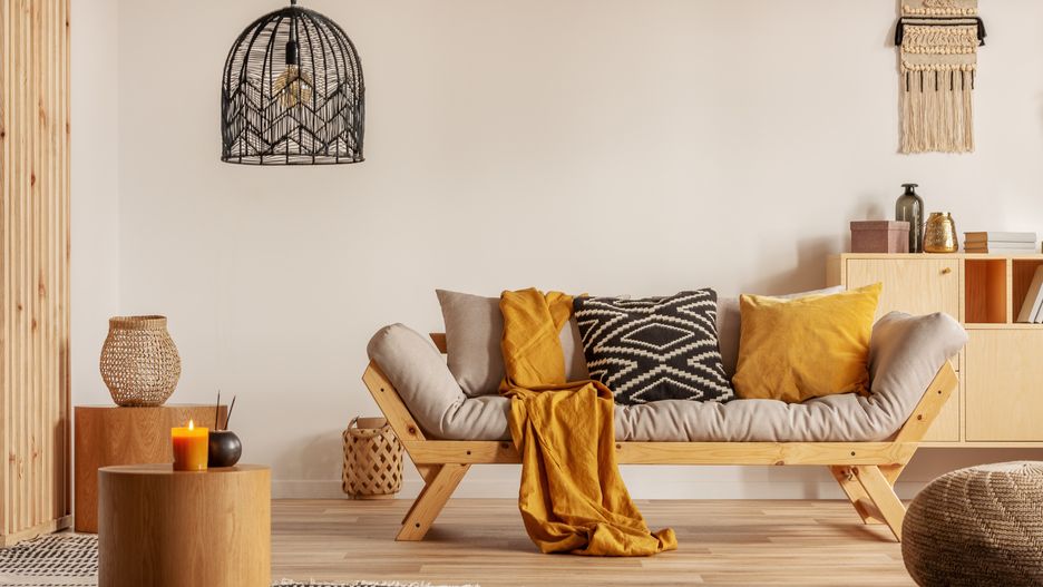Scandinavian sofa with pillows and dark yellow blanket in bright living room interior with black chandelier