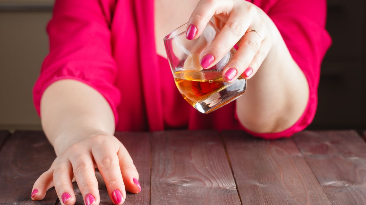 Woman drink whiskey from glass on wooden table