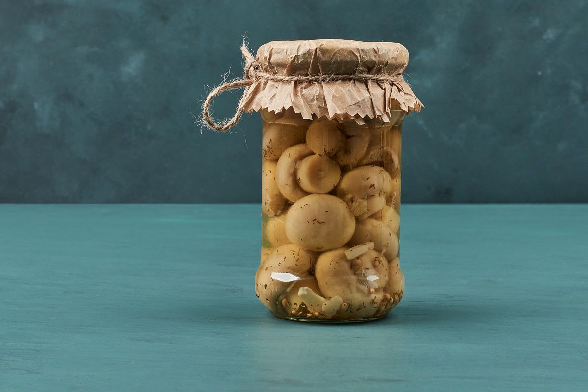 Pickled mushrooms in a glass jar on blue table. High quality photo