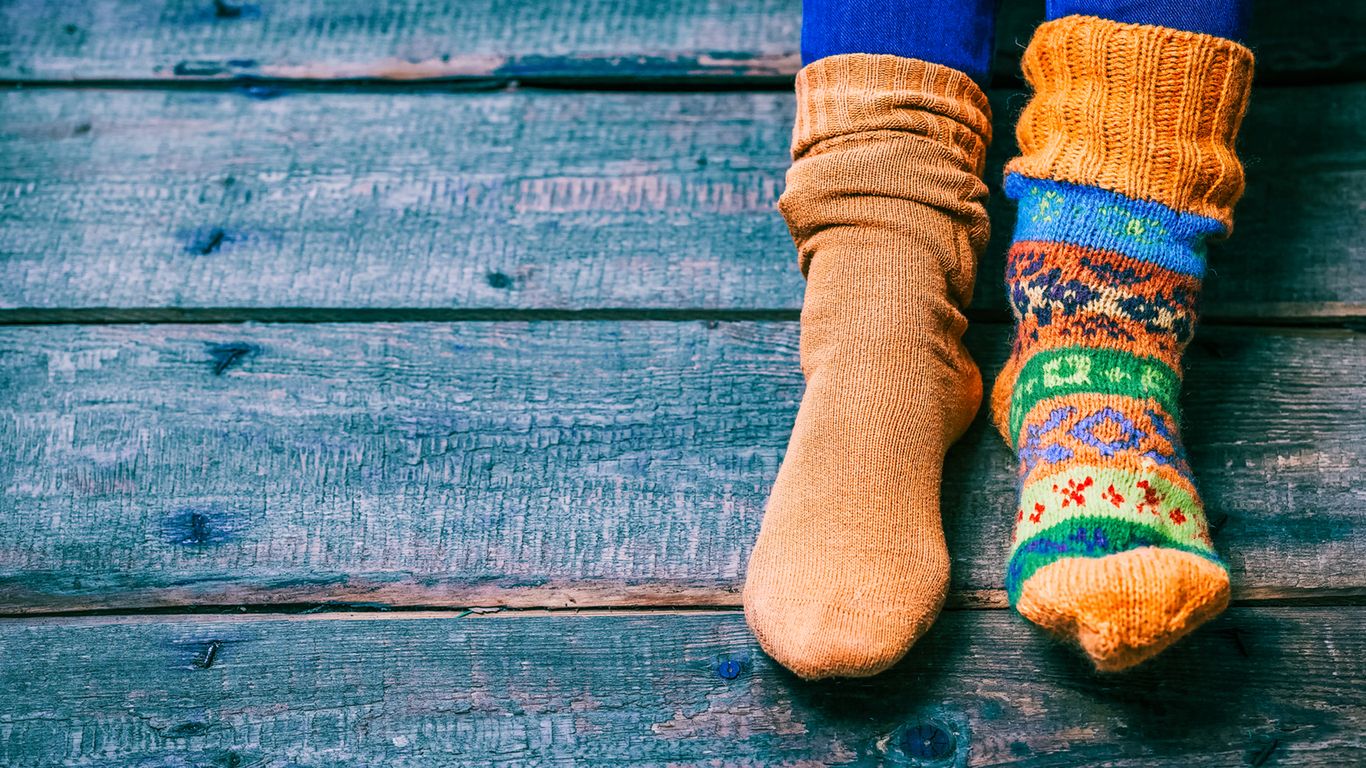 Female feet wearing odd wool socks on the wooden floor. Closeup view 