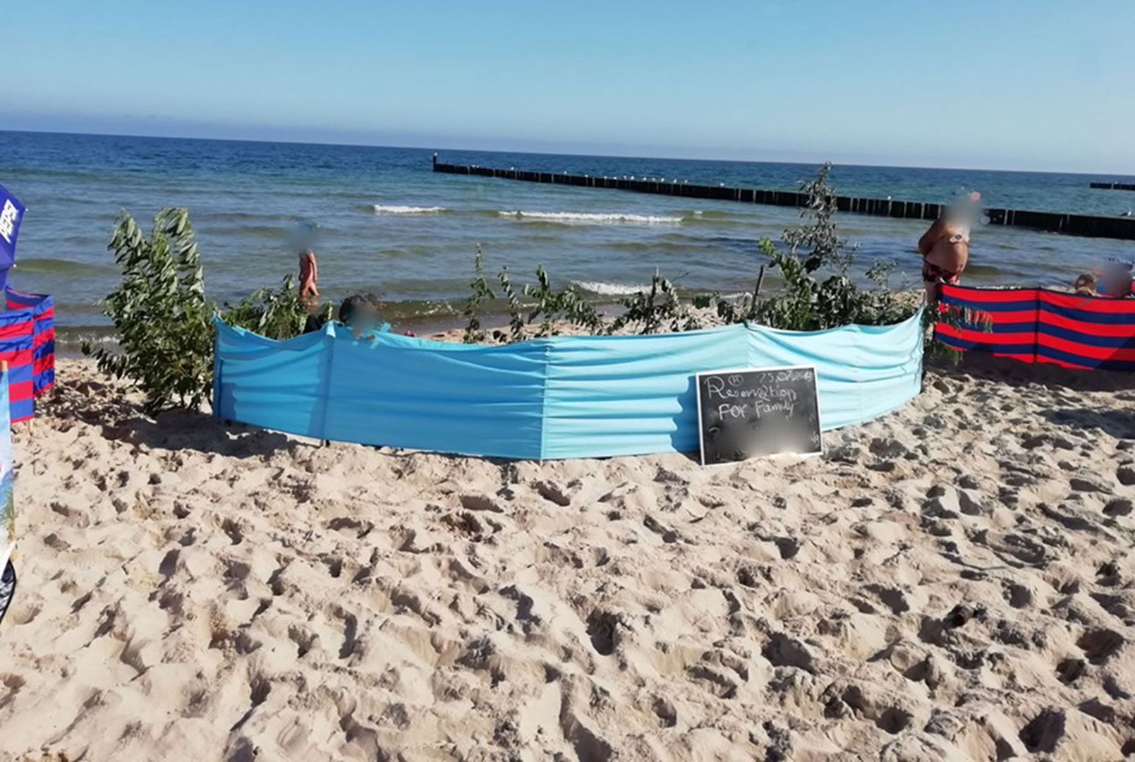Gałęzie i konary z wydm, a obok tabliczka z informacją o "rezerwacji" na plaży w Ustroniu Morskim