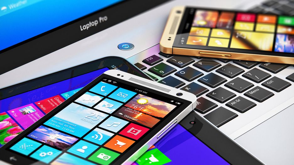 Mobility and modern internet business communication technology concept: macro view of office laptop or notebook, tablet computer PC and black glossy touchscreen smartphones with color interfaces with icons and buttons