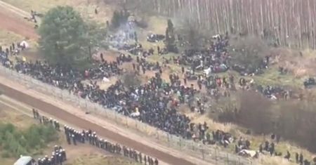 Setki  migrantów z plecakami i śpiworami przy granicy z Polską. Obok uzbrojeni ludzie w mundurach.