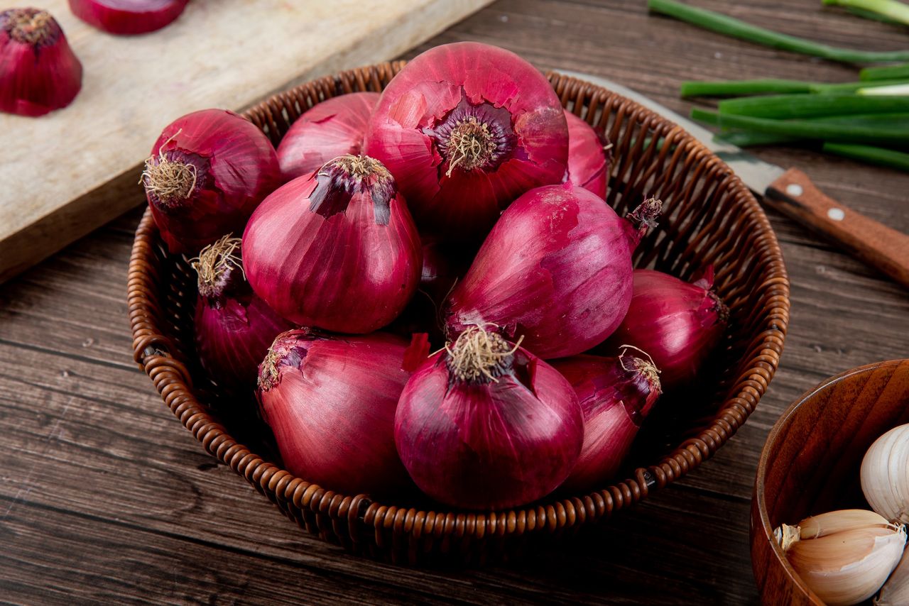 side view of basket full of red onions on wooden background