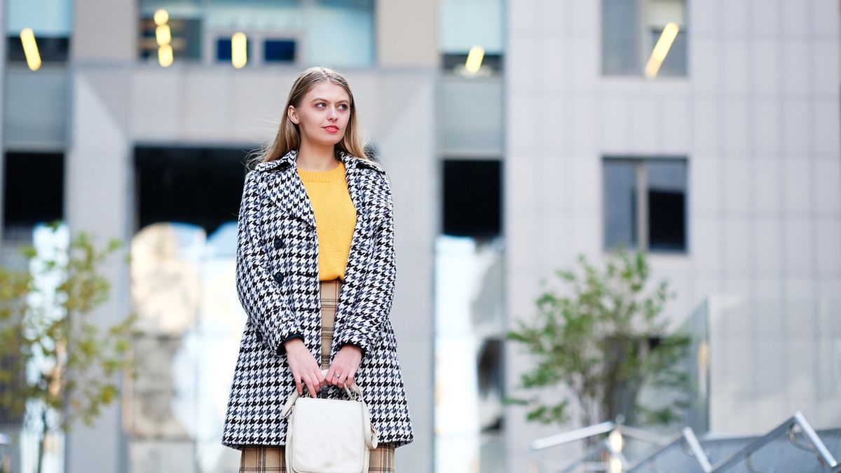 Blond hair young woman in check skirt against modern building. Street fashion style concept.