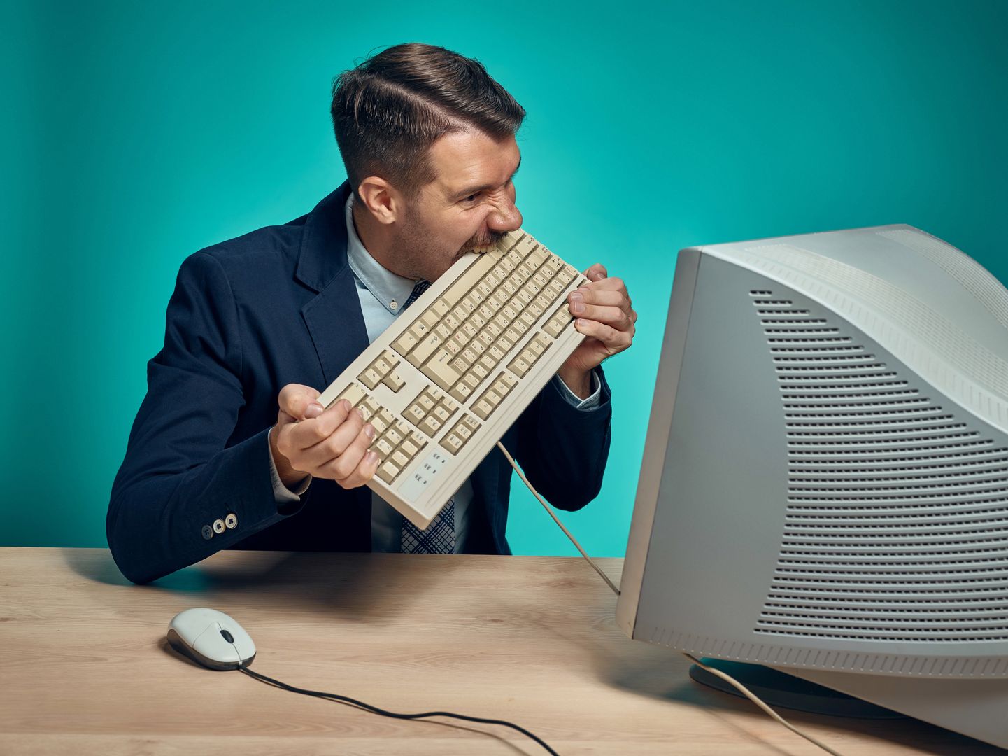 Angry fury businessman breaking keyboard against a blue studio background
