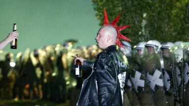 Punk z butelką piwa przed kordonem policji