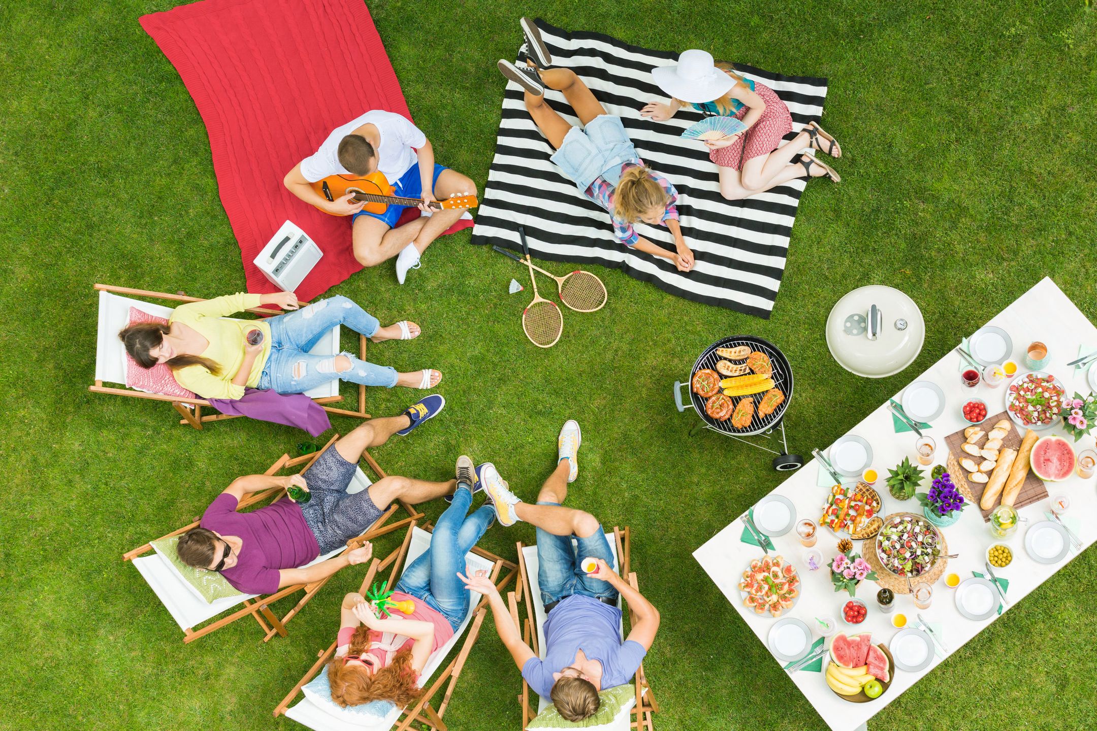 Top view of group of young friends having summer barbecue party in the backyard with grill and table full of delicious food 