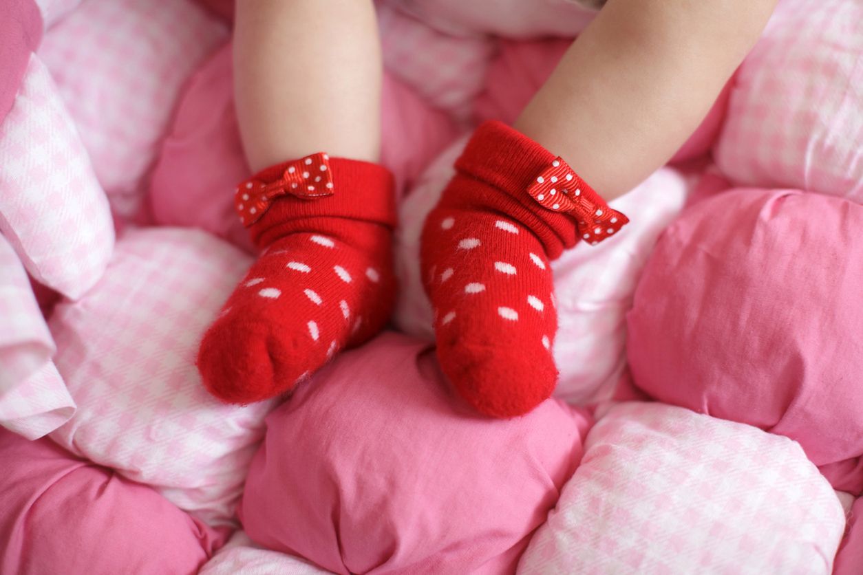 Close up of babies feet wearing red cotton socks, pink background, selective focus 