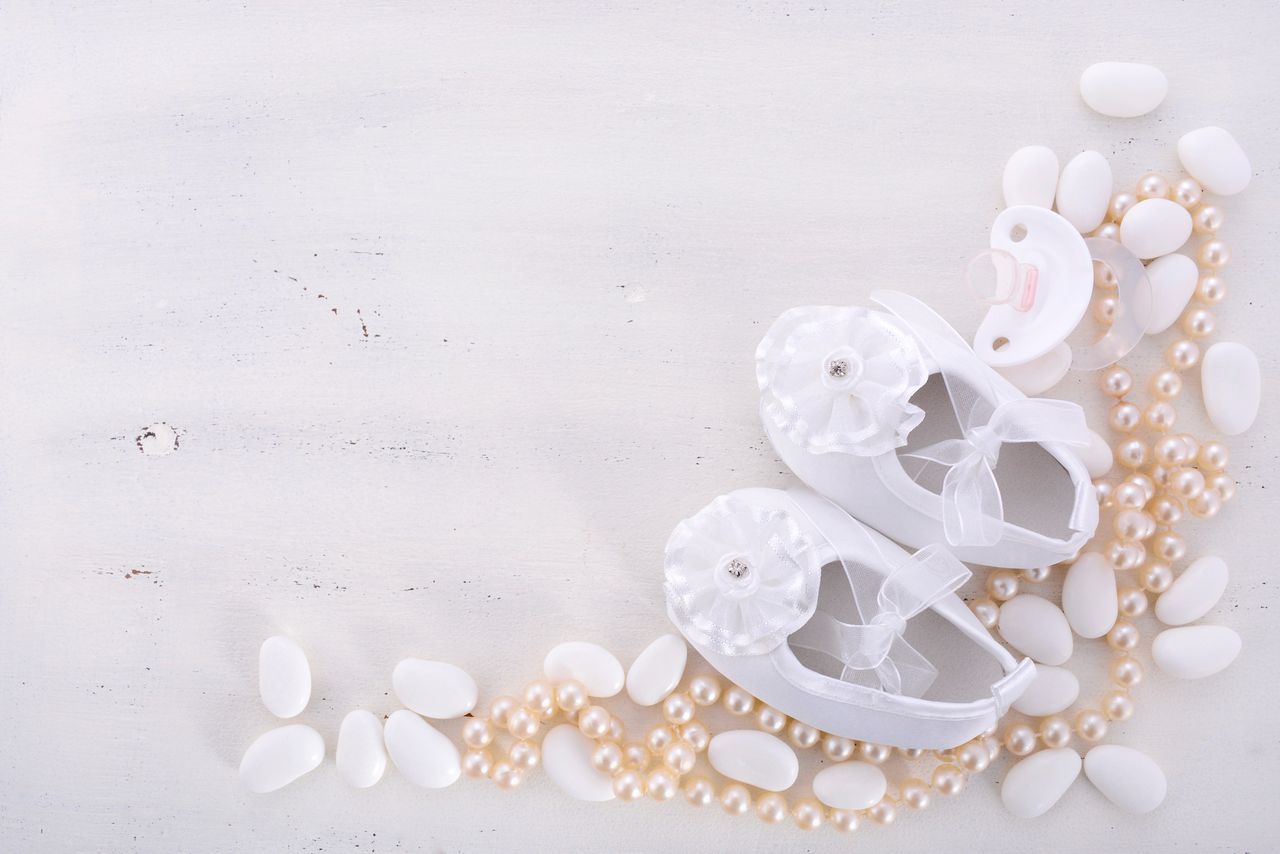 <p>Baby shower neutral white background with baby booties, pearls, and sugar almonds on shabby chic rustic wood table, with copy space.</p>