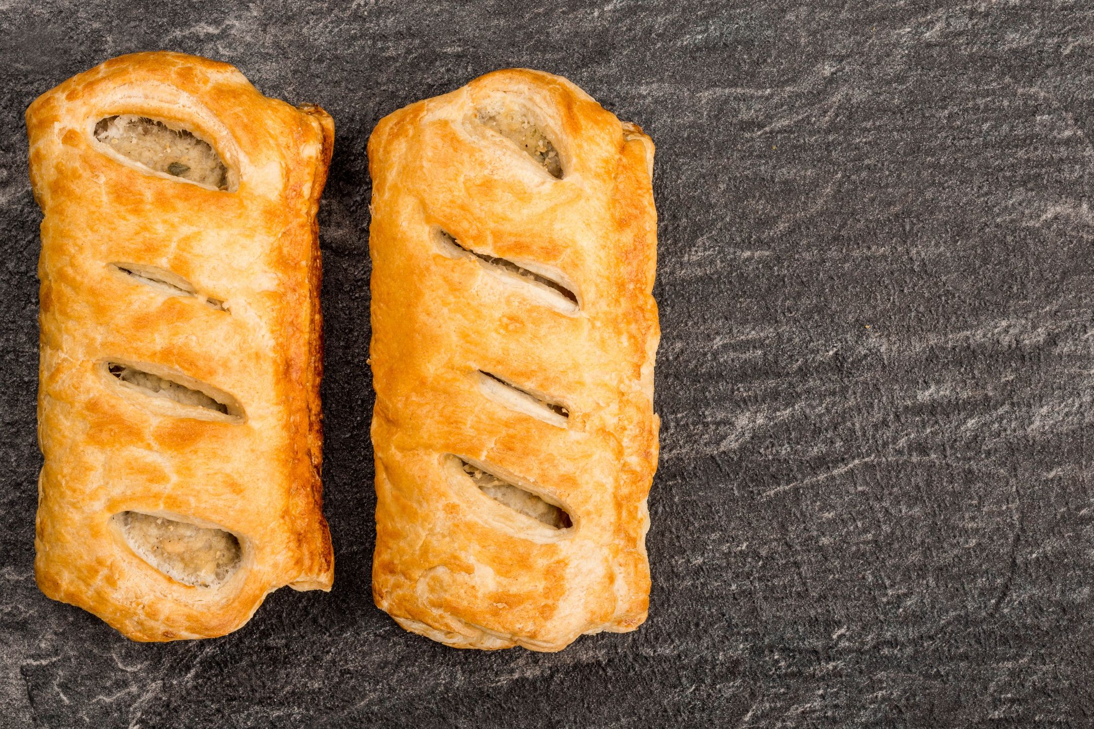 Sausage Rolls in Pastry On A Black Slate Kitchen Tile With Copy Space 