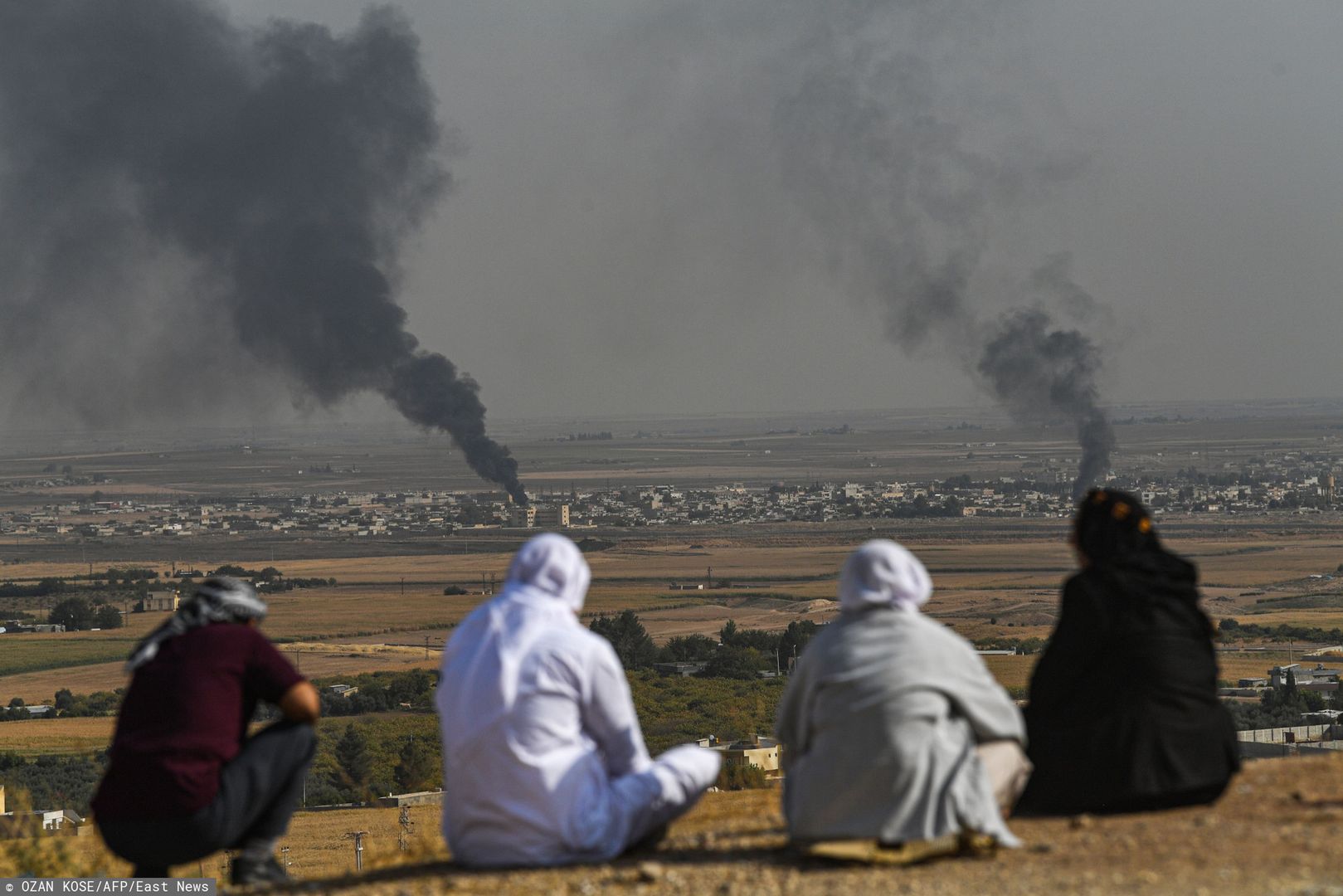 Atak Turcji na Syrię. Ludzie patrzą, jak dym unosi się z syryjskiego miasta Ras al-Ain, na zdjęciu wykonanym po tureckiej stronie granicy, w Ceylanpinar, 11 października br.