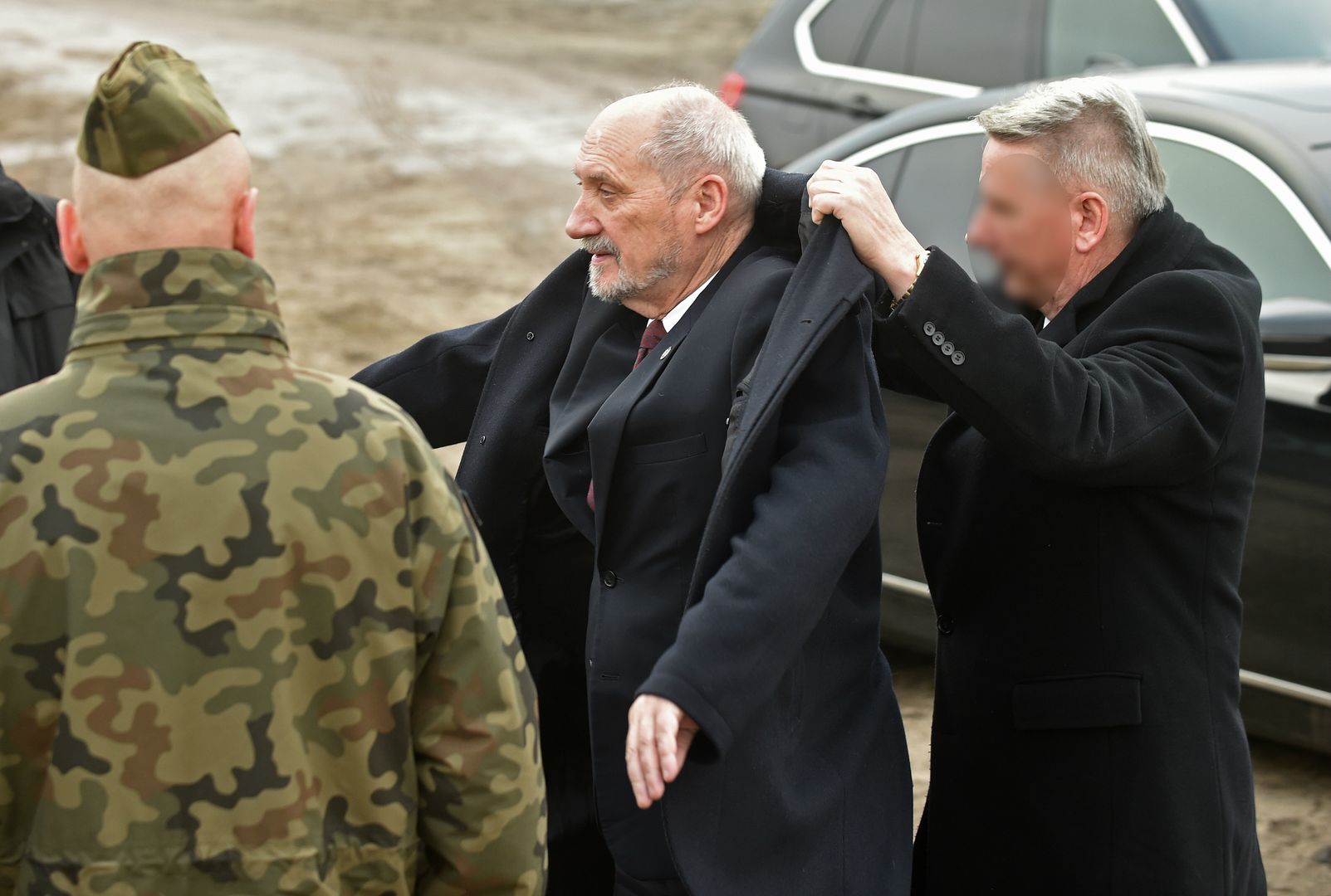 Antoni Macierewicz zakłada płaszcz. Nie sam. Ma od tego ludzi