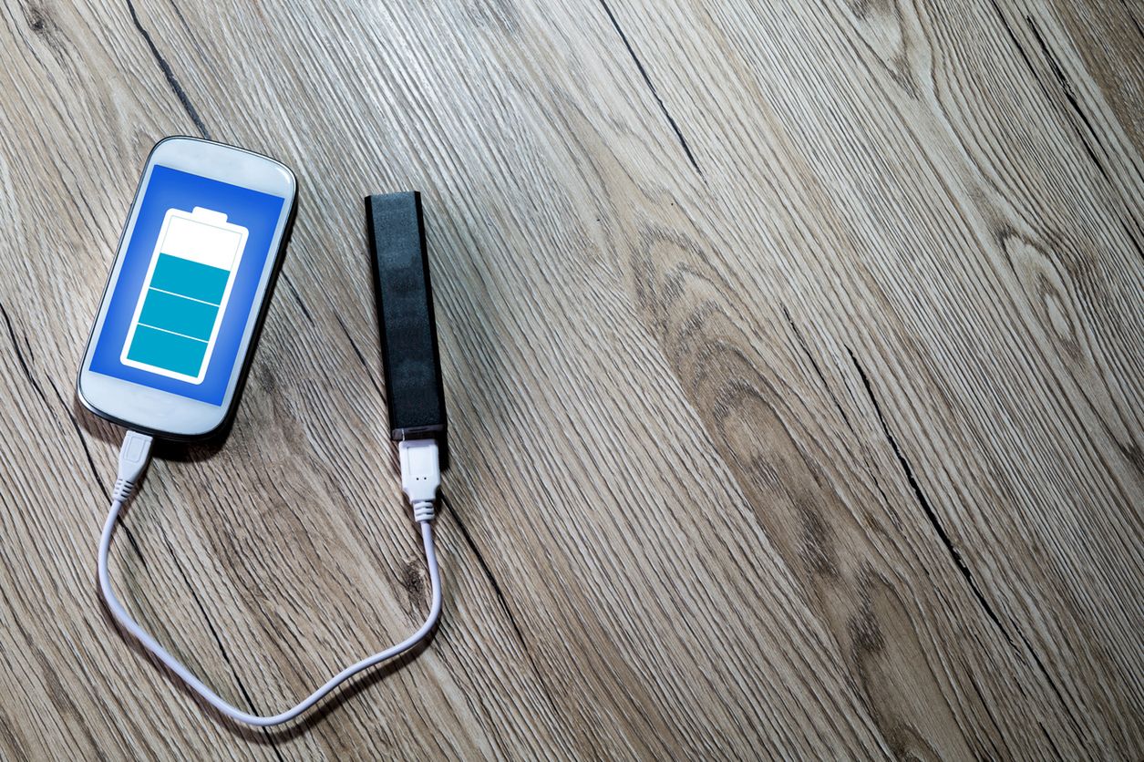 a white smartphone charging with a powerbank on a desk. 