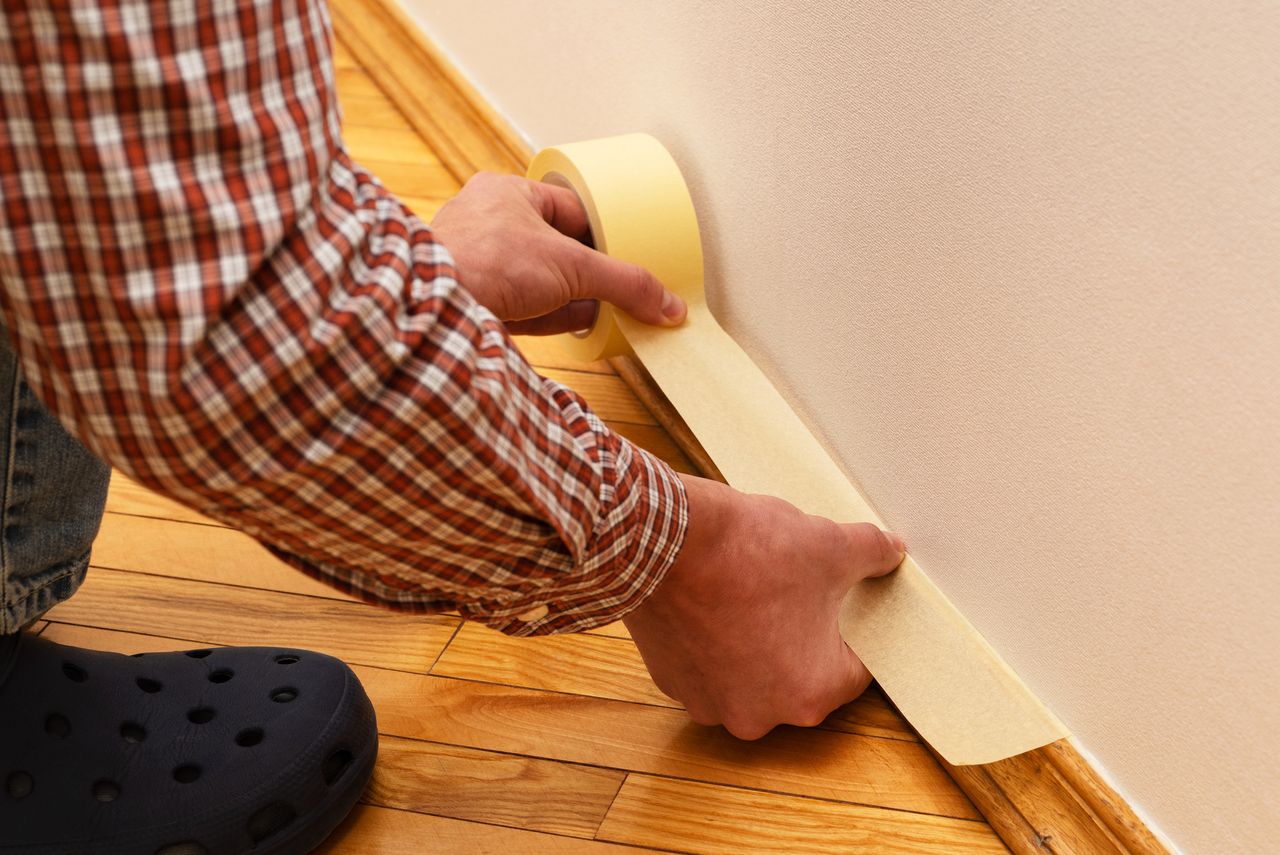 House Painter glues masking tape to the baseboard to protect it from paint