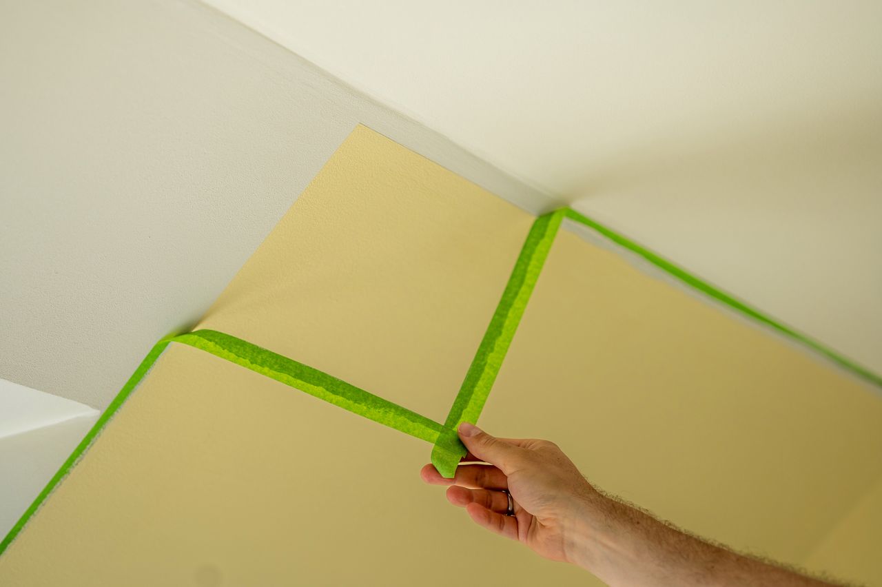 Painter removes masking tape and creates a sharp border between a yellow and white painted part of a wall.