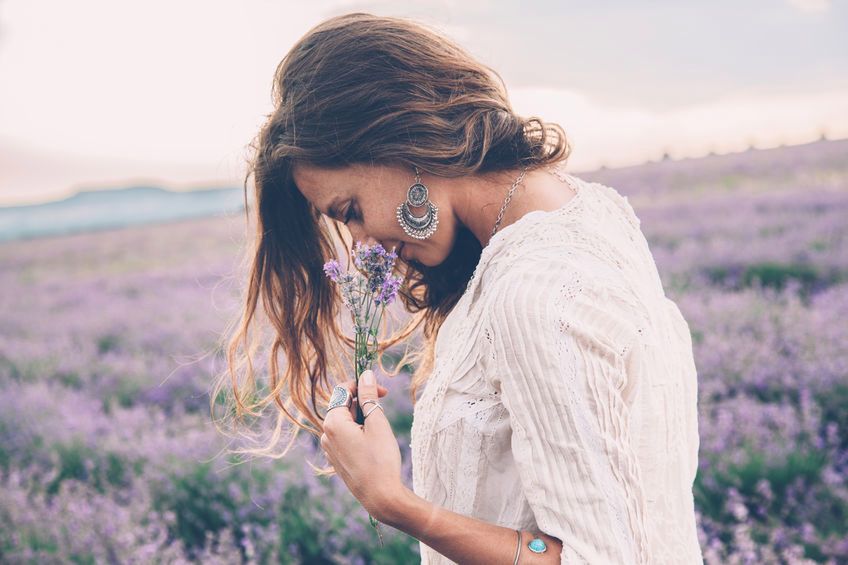 Beautiful model walking in spring or summer lavender field in sunrise backlit. Boho style clothing and jewelry. 