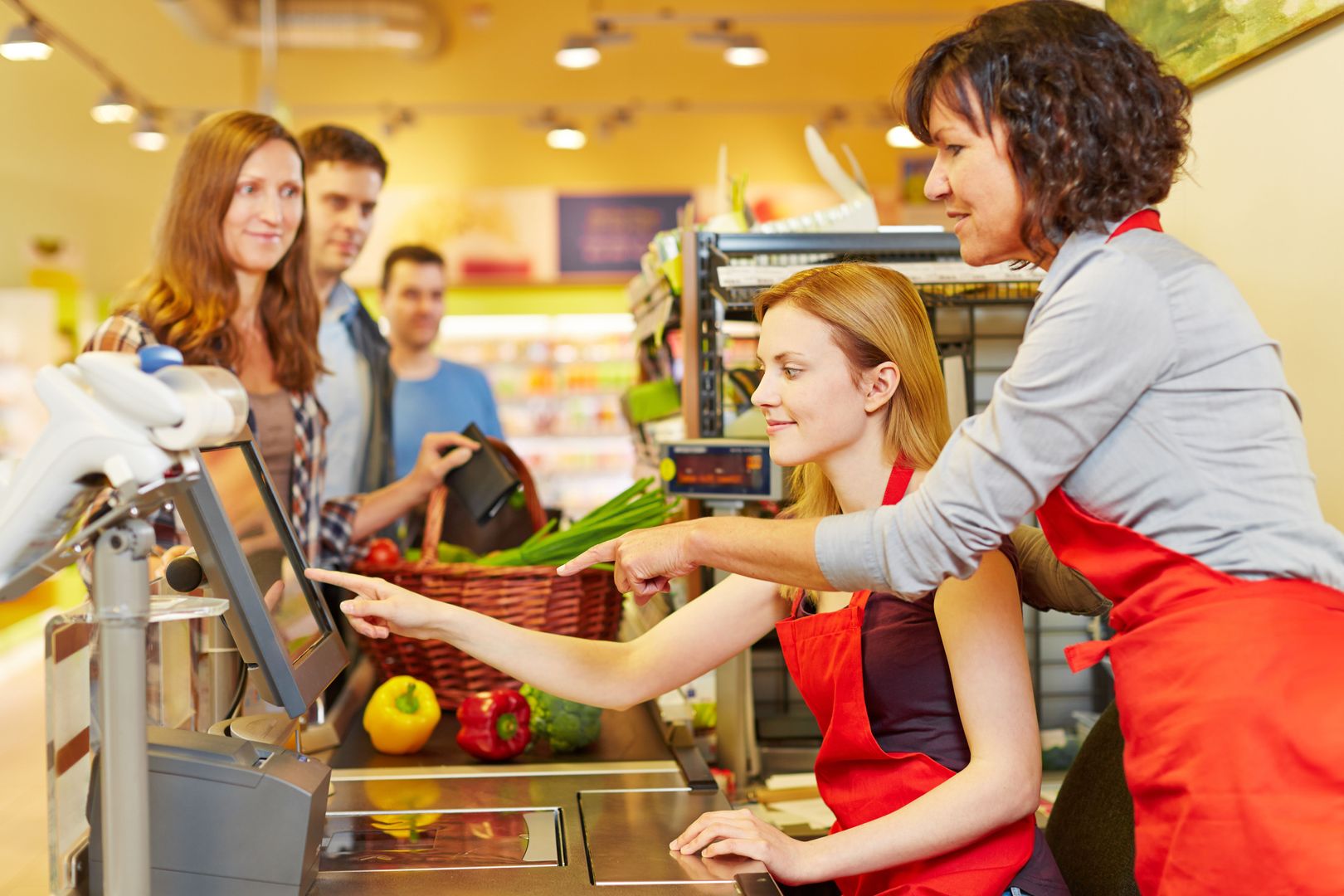 ��ltere Verk��ufer hilft einer neuen Kassiererin an der Kasse im Supermarkt