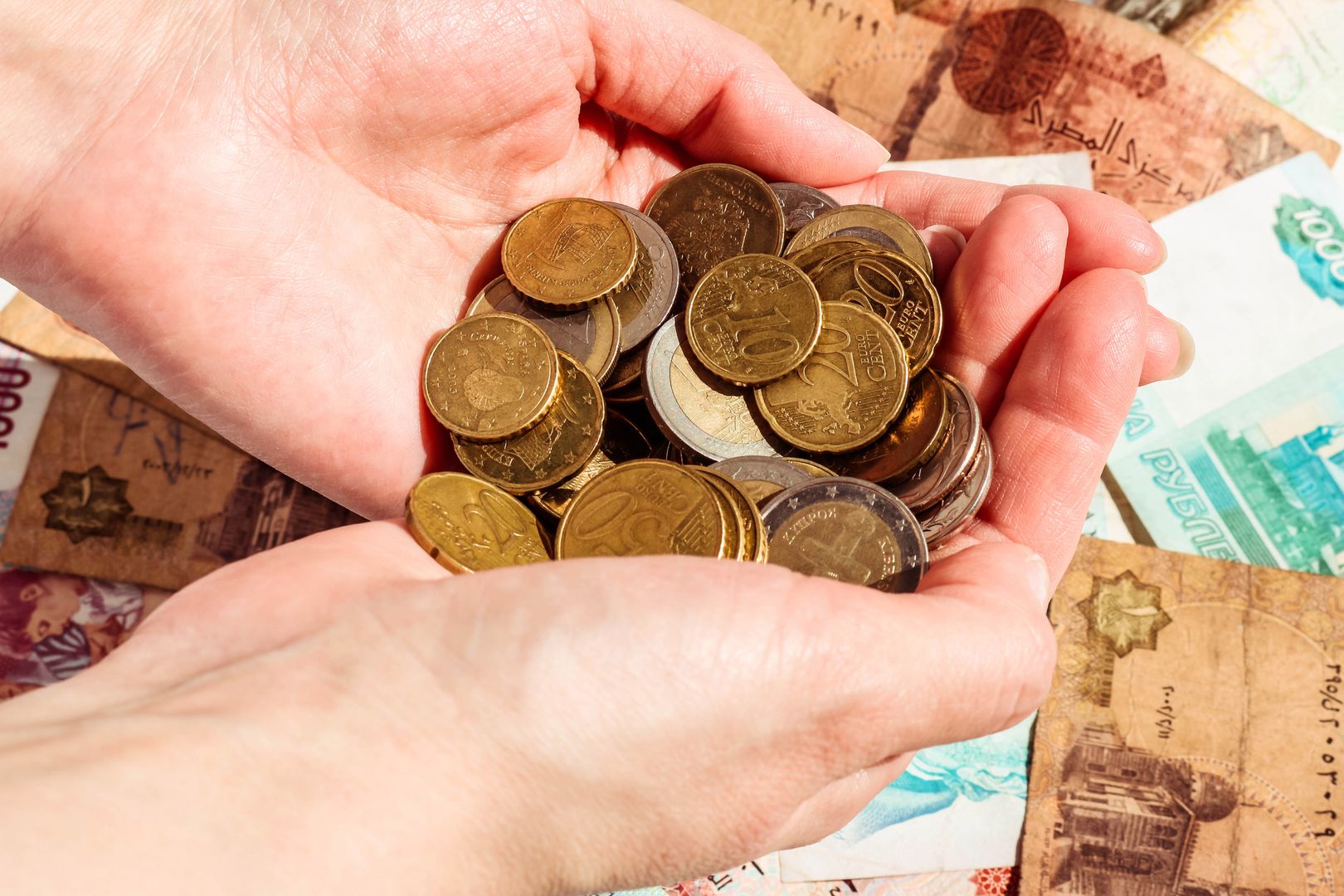 Female hands with money over banknote background. Euro coins Euro cents.