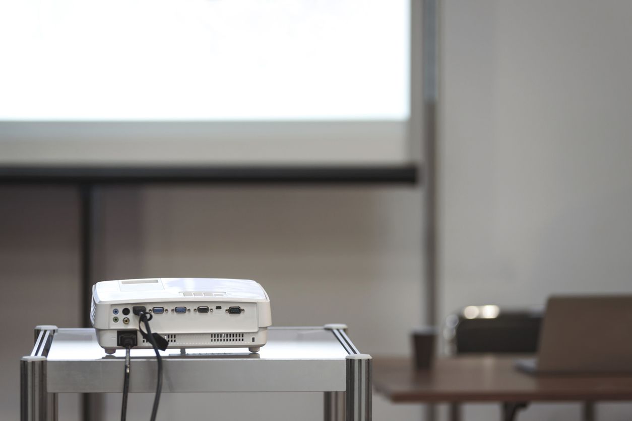 White multimedia projector in a conference room with blured projection screen and a lecturer desk on the background (reduced tone) 