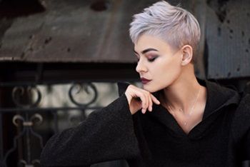 Young beautiful girl with short gray hair in a black jacket and aggressive leather boots, fashionable shooting on the street near the brick wall of the house 
