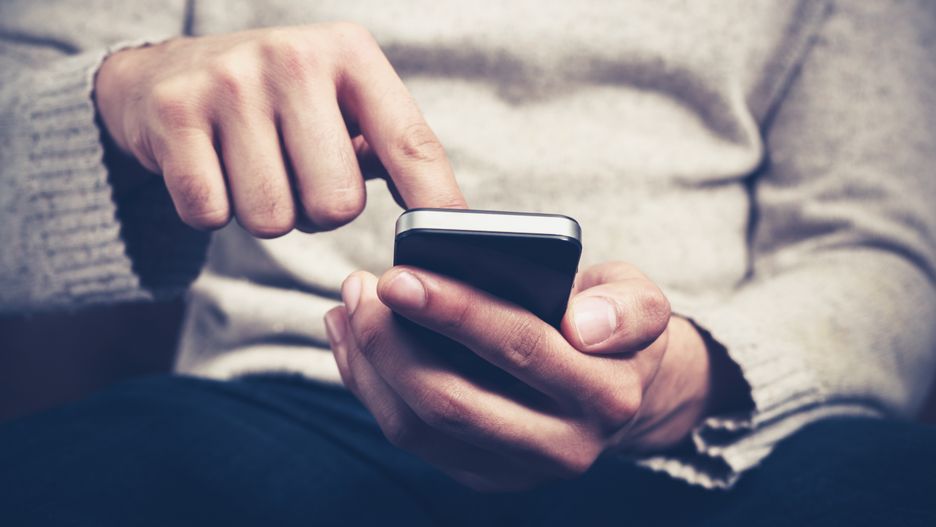 Closeup on a man's hands as he is sitting on a sofa and using a smartphone