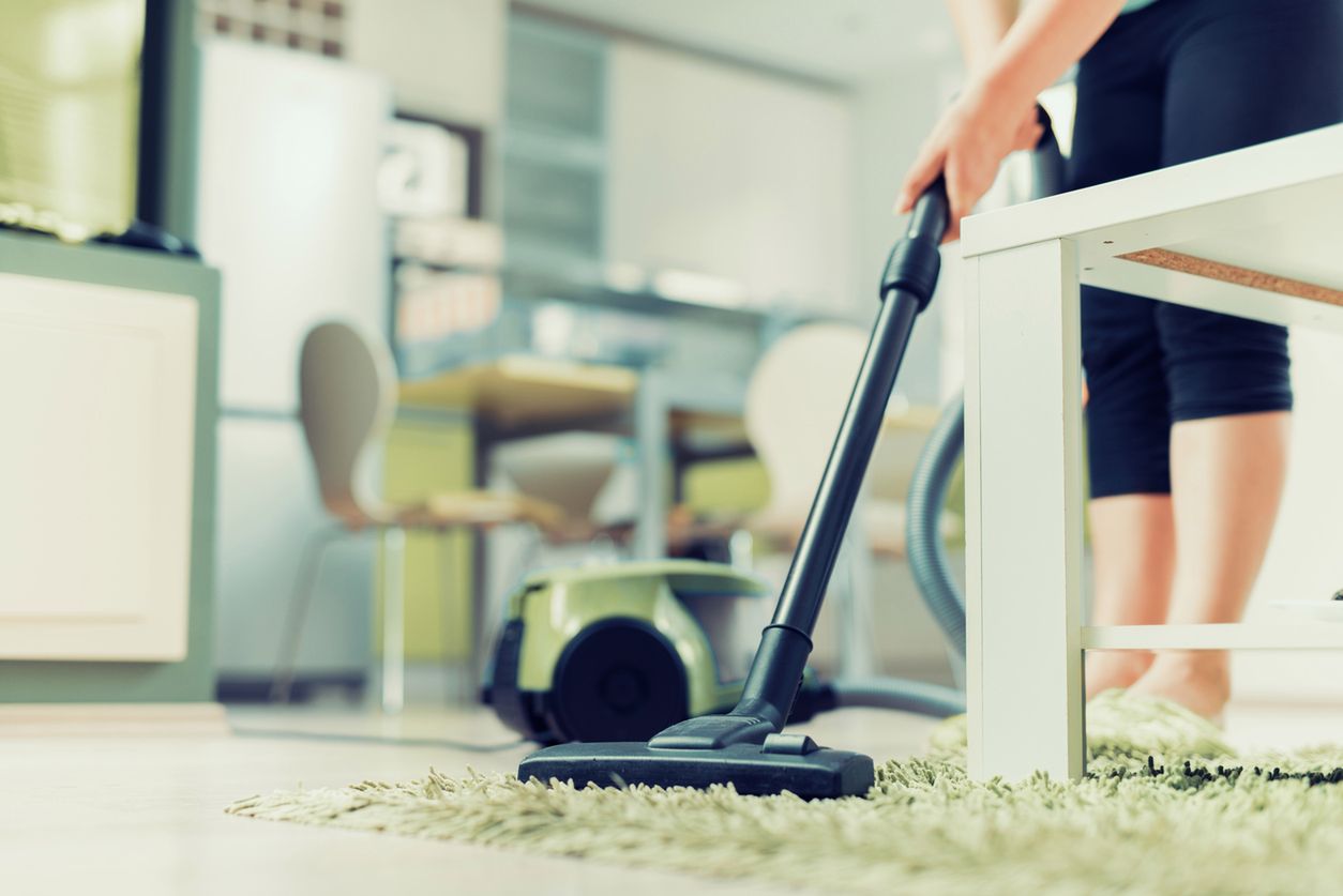 Close up of woman with legs vacuum cleaner cleaning carpet at home. 