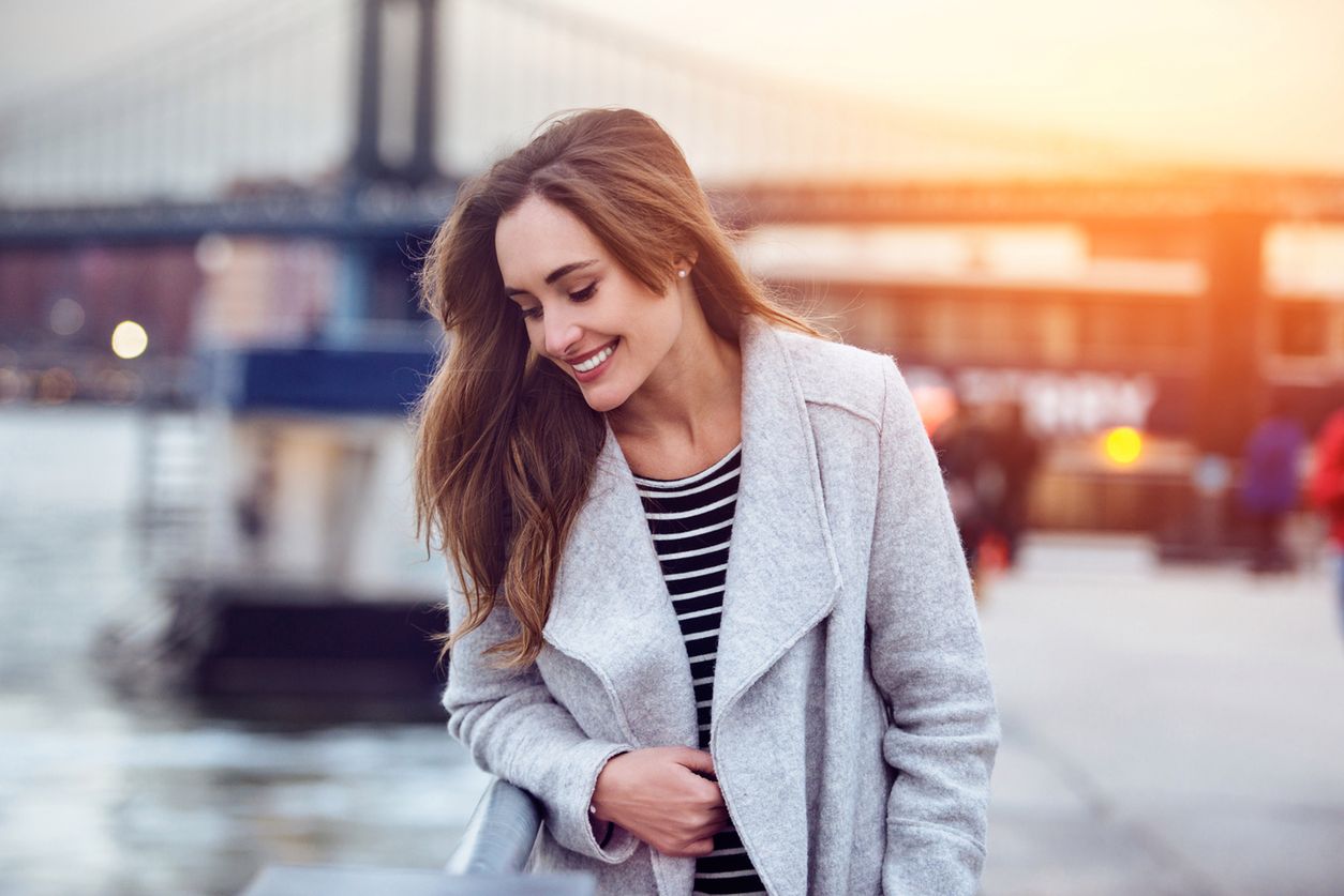 Beautiful happy woman walking near East River in New York City and looking down 