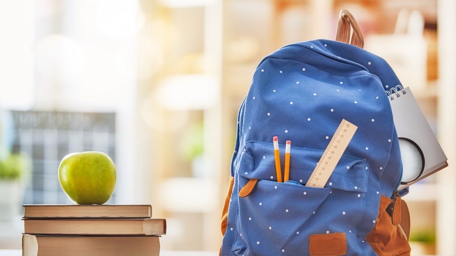 Back to school and happy time! Apple, pile of books and backpack on the desk at the elementary school. 