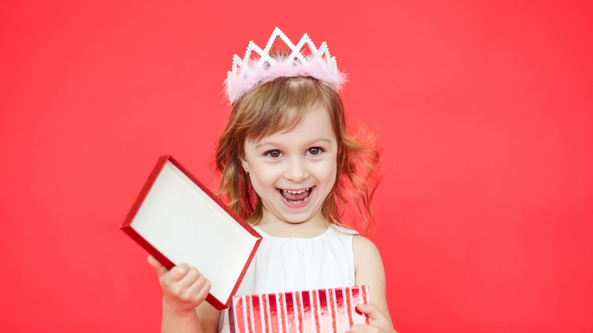 Happy Kid girl opening a gift box isolated on red background. Surprised cute little girl with a red wrapped present
